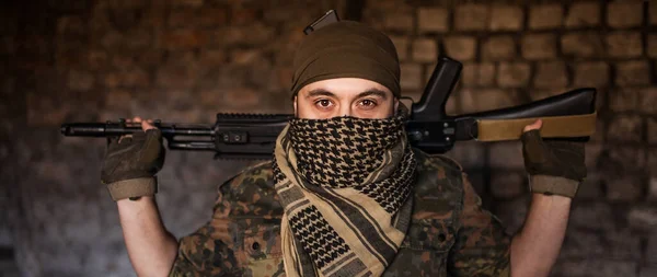 Elinde silahlarla milli keffiyeh 'den başlıklı Arap erkek asker. Tuğla duvarın arkasında ateşli silahları olan bir Müslüman.