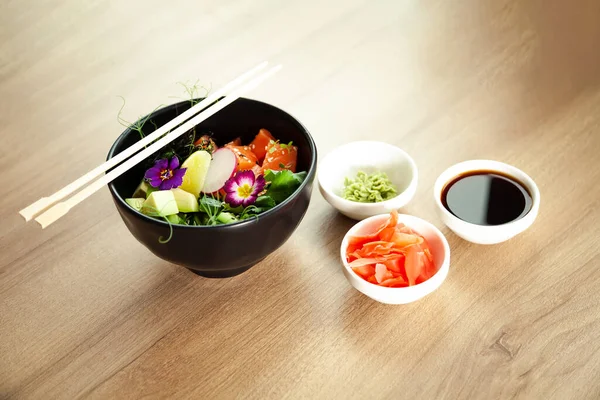 Poke salade met zalm in een kom naast wasabi en gember. Ingrediënten verse zalm, avocado, komkommer, rijst, Tamarindesaus, mangosaus, nori limoensesamzaad koriander. Aziatische zeevruchten salade concept — Stockfoto