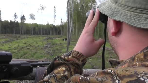 L'uomo cacciatore guarda attraverso il binocolo. Uomo cacciatore con una pistola guardando attraverso binocoli nella foresta a guardare gli animali selvatici — Video Stock