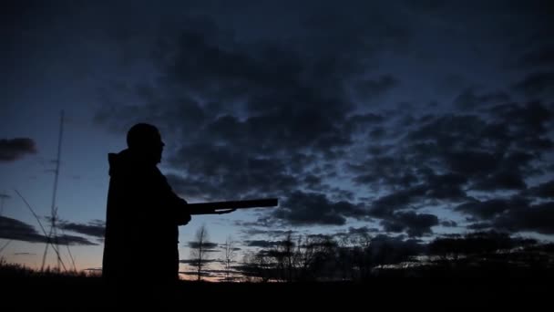 Silhouette eines Jägers bei Nacht mit einem Gewehr. Silhouette eines Jägers mit einem Gewehr vor dem Hintergrund des Sonnenuntergangs. Ein Mann mit einem Gewehr vor dem Hintergrund des Abendhimmels und des Flusses auf der Jagd — Stockvideo