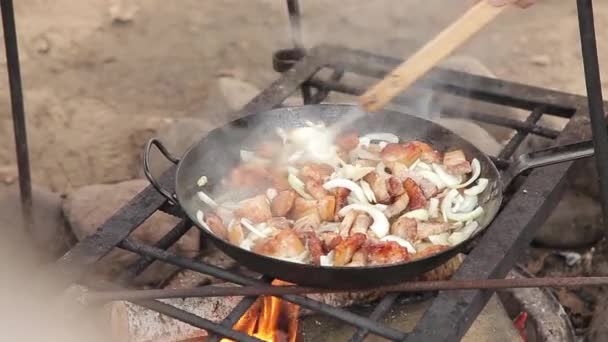 Poêle à frire avec bacon sur le feu. Une grande poêle en fonte avec des morceaux de ventre de porc sur un feu ouvert sur un crémaillère dans les bois. Nourriture dans la nature. Cuisiner de la nourriture sur la route. Pique-nique — Video