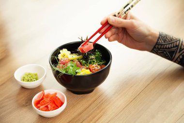 Çubuklu ton balıklı dürtme salatası yiyen bir adam. Ton balıklı salatayı bir kaseye koy. Restoranda salata yiyen genç bir adam. Asya deniz ürünleri salatası konsepti.