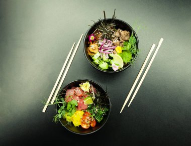 Masada ton balıklı salatalar ve kaselerde sığır eti. Gri arka planda çubuklarla iki kase salata. Asya deniz ürünleri salatası konsepti