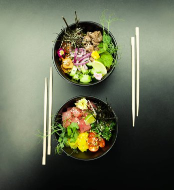 Masada ton balıklı salatalar ve kaselerde sığır eti. Gri arka planda çubuklarla iki kase salata. Asya deniz ürünleri salatası konsepti