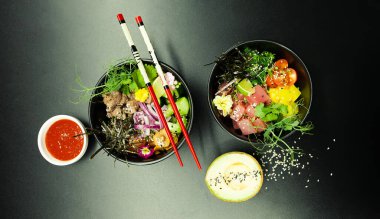 Masada ton balıklı salatalar ve kaselerde sığır eti. Gri arka planda çubuklarla iki kase salata. Asya deniz ürünleri salatası konsepti