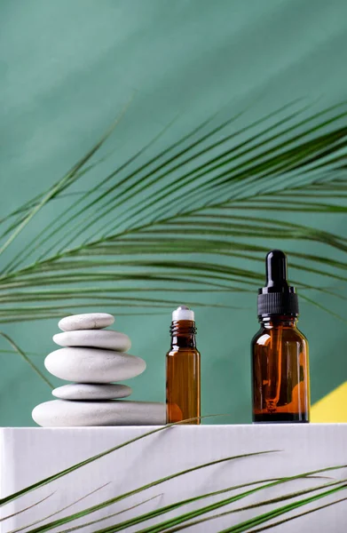 Roller bottle and dropper bottle and stones on podium against the green background. Beauty products packaging. Spa concept