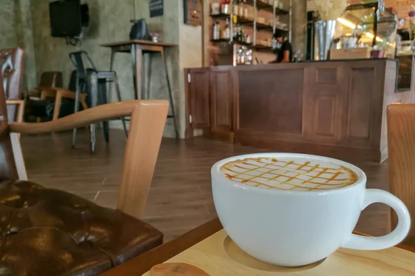 Caramelo Macchiato café caliente en taza blanca con fondo de la barra de café — Foto de Stock
