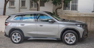 Çağdaş gümüş renkli, parlak çizgileri, siyah çatısı ve kendine özgü LED stop lambaları olan bir BMW bir garaj yolunda park halinde.