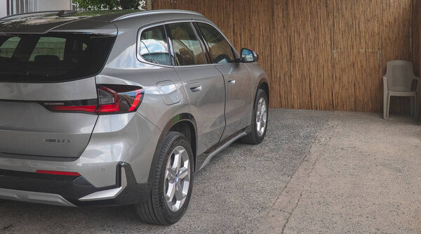 A modern silver BMW with sleek lines, a black roof, and distinctive LED rear lights, is parked in a driveway