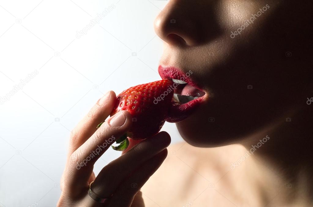 Sexy red lips eating strawberry. Hot desire. White background.