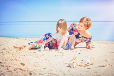 Genç ve güzel kadın ve küçük kızı deniz kıyısı üzerinde oturuyor