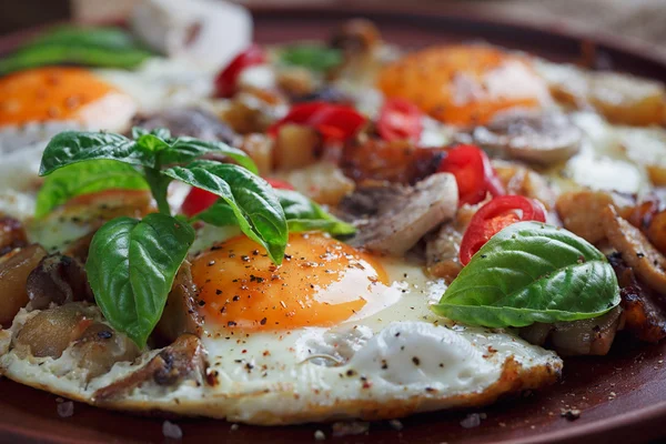 Fried eggs with mushrooms, tomatoes and basil on rustic wooden t