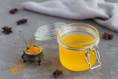 Ev yapımı Ghee veya kavanozda tereyağı ve gri beton arka planda zerdeçal tozu..