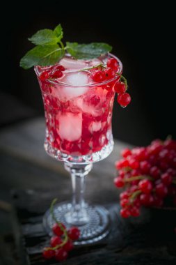 Beyaz köpüklü şaraplı yaz içkisi. Ev yapımı taze meyve kokteyli ya da şampanya, kırmızı frenk üzümü, buz küpleri ve koyu ahşap arka planda naneli yapraklar..