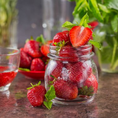 Kahverengi arka planda cam kavanozda taze çilek ve nane yaprağı yığını. Sağlıklı beslenme ve diyet gıda kavramı.