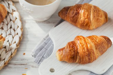 Taze kruvasan ve beyaz ahşap arka planda bir fincan kahve ile nefis bir kahvaltı. Lezzetli Pişirme