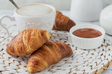 Taze kruvasanla nefis bir kahvaltı ve beyaz ahşap arka planda reçelle servis edilen bir fincan kahve. Lezzetli Pişirme