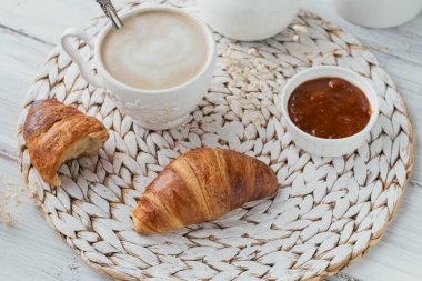 Taze kruvasanla nefis bir kahvaltı ve beyaz ahşap arka planda reçelle servis edilen bir fincan kahve. Lezzetli Pişirme