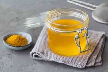 Ev yapımı Ghee veya kavanozda tereyağı ve gri beton arka planda zerdeçal tozu..