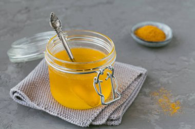 Ev yapımı Ghee veya kavanozda tereyağı ve gri beton arka planda zerdeçal tozu..