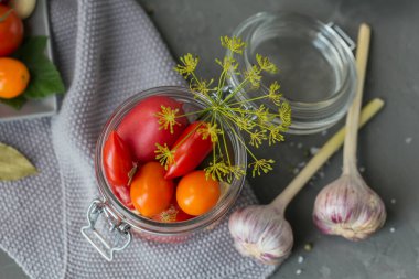 Taze ve turşulu domatesleri, baharatları ve sarımsağı gri beton masada muhafaza etmek. Sağlıklı mayalanmış yiyecek. Ev yapımı sebze konservesi. Üst görünüm
