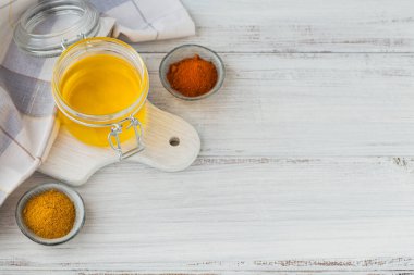 Beyaz ahşap masa üzerinde ev yapımı Ghee ya da tereyağı kavanozu, zerdeçal ve kırmızı biber tozu.