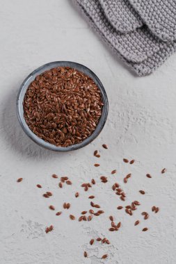 Kahverengi keten tohumu veya keten tohumu açık gri arka planda küçük bir kasede.
