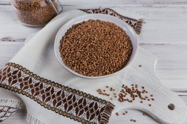 Pişmemiş organik karabuğday taneleri beyaz ahşap arka planda bir kasede. Sağlıklı ve diyet gıda konsepti.