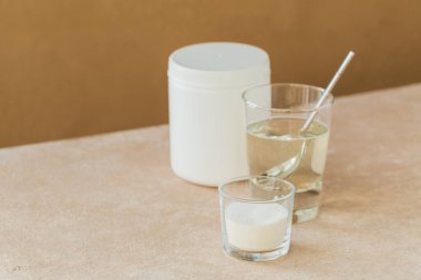 Kolajen içeren cam suda çözünmüş ve kolajen protein tozu açık bej masa üzerinde. Sağlıklı yaşam tarzı kavramı.
