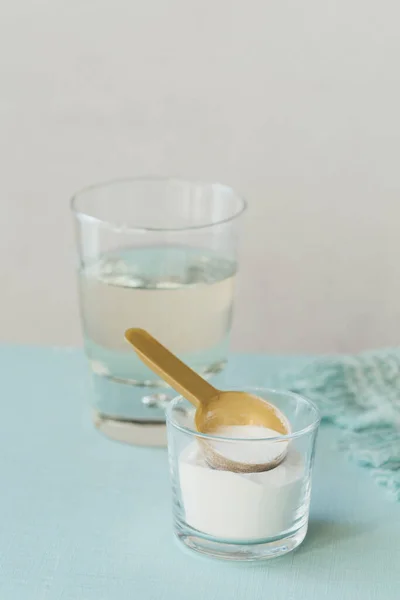 Kolajen içeren cam suda çözünmüş ve açık mavi masada kolajen protein tozu var. Sağlıklı yaşam tarzı kavramı.