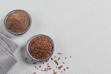 Kahverengi keten tohumu ve toprak ya da ezilmiş keten tohumu ya da açık gri arka planda küçük bir kasede keten tohumu. Üst görünüm