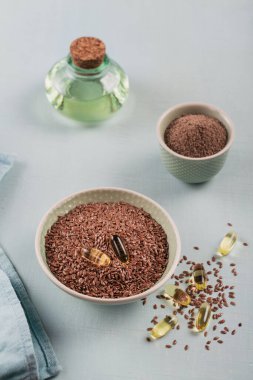 Kahverengi keten tohumu veya keten tohumu ve toprak ya da açık mavi arka planda omega yağlı küçük kâse ve jelatin kapsüllerde ezilmiş keten tohumu..