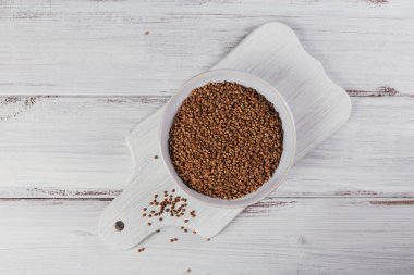 Beyaz ahşap arka planda bir kase kuru çiğ karabuğday inliyor. Karabuğday lapası pişirme kavramı.