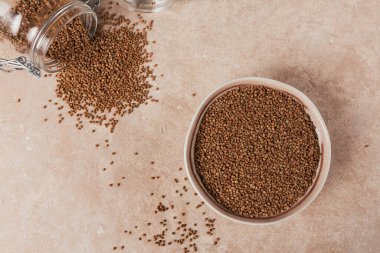 Pişmemiş organik karabuğday taneleri bir kasede ve açık bej arka planda cam kavanozda. Sağlıklı ve diyet gıda konsepti.