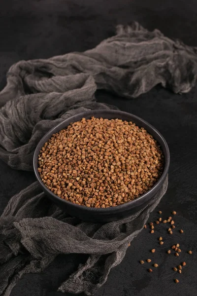 Grano de trigo sarraceno orgánico sin cocer en un tazón sobre un fondo negro. Concepto de alimentos saludables y dietéticos. — Foto de Stock