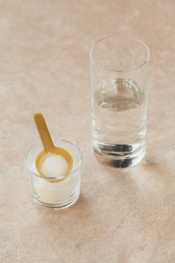 Kasede kolajen tozu, bir bardak su ve açık bej arka planda ölçü kaşığı. Fazladan protein alımı. Doğal güzellik ve sağlık takviyesi konsepti.