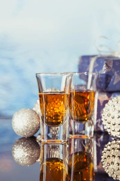 Two glasses of whiskey or bourbon with Christmas decoration on light bokeh background. New Year, Christmas and winter holidays whiskey mood concept