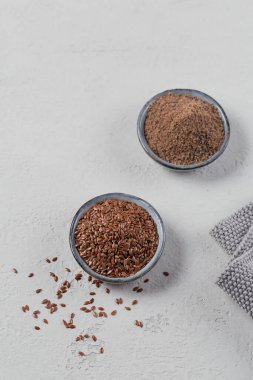 Kahverengi keten tohumu ve toprak ya da ezilmiş keten tohumu ya da açık gri arka planda küçük kasede keten tohumu..