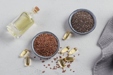 Kahverengi keten tohumu veya keten tohumu ve chia küçük kasede ve açık gri arka planda omega yağlı jelatin kapsüller. Üst görünüm