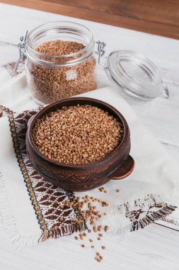 Beyaz ahşap arka planda bir kase kuru çiğ karabuğday inlemesi. Karabuğday lapası pişirme kavramı.