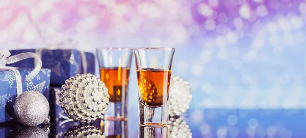 Two glasses of whiskey or bourbon with Christmas decoration on light bokeh background. New Year, Christmas and winter holidays whiskey mood concept