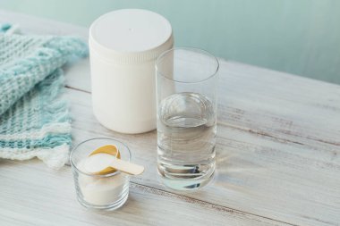 Kasede kolajen tozu, bir bardak su ve açık mavi zemin üzerinde kaşık ölçüsü. Fazladan protein alımı. Doğal güzellik ve sağlık takviyesi konsepti.