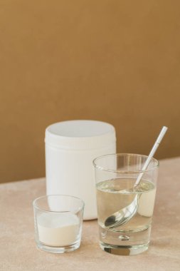 Kolajen içeren cam suda çözünmüş ve kolajen protein tozu açık bej masa üzerinde. Sağlıklı yaşam tarzı kavramı.