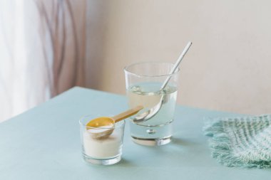 Kolajen içeren cam, açık mavi bir masada suda çözünmüş ve kolajen protein tozu. Sağlıklı yaşam tarzı kavramı.