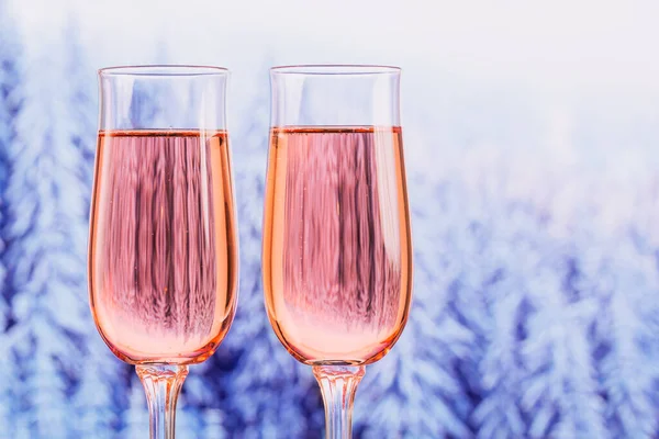 Dos copas de champán rosa con bokeh bosque nevado de invierno como fondo. Cena romántica. Concepto de vacaciones de invierno, Navidad o Año Nuevo. —  Fotos de Stock