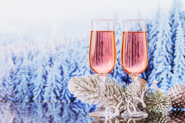 Dos copas de champán rosa y decoración de Navidad o Año Nuevo con bokeh bosque nevado de invierno como fondo. Cena romántica. Concepto de vacaciones de invierno. —  Fotos de Stock