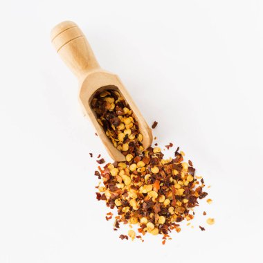 Ahşap kepçe dolusu ezilmiş kırmızı kırmızıbiber, kurutulmuş kırmızı biber ve beyaz arka planda izole edilmiş tohumlar. Yemek pişirmek için ev yapımı baharatlar..