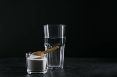 Kasede kolajen tozu, bir bardak su ve siyah arka planda kaşık ölçüsü. Fazladan protein alımı. Doğal güzellik ve sağlık takviyesi konsepti.