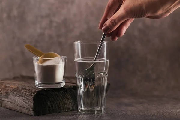Kolajen içeren cam su ve kolajen protein tozunda çözünmüş. Kadının eli kaşığı tutuyor. Sağlıklı yaşam tarzı kavramı.