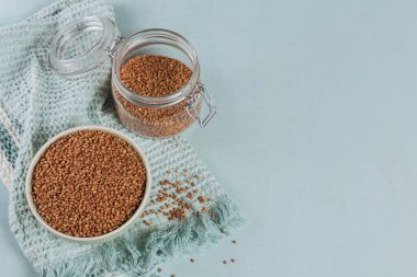 Açık mavi arka planda bir kase çiğ karabuğday Groats ve cam kavanoz. Karabuğday lapası pişirme kavramı.